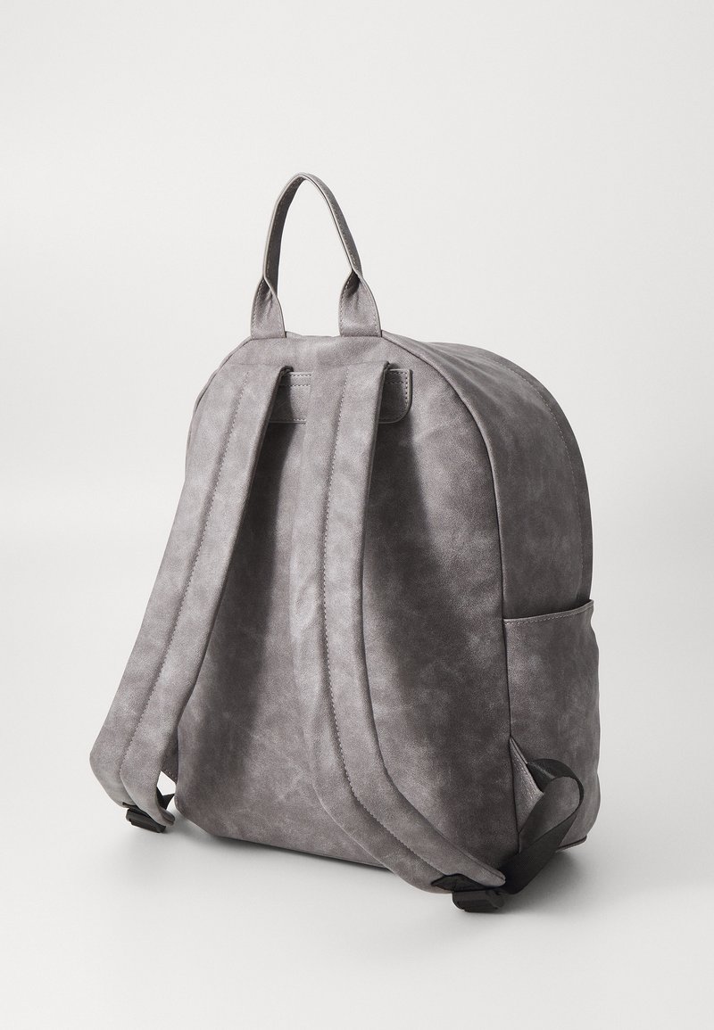 Mochila gris con una superficie suave y texturizada, doble correa para los hombros, asa superior y bolsillo lateral, con un diseño redondeado.