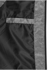 Doublure intérieure en tissu noir d'une veste avec une bande horizontale en tissu gris et une bordure en tissu gris le long d'un bord de fermeture éclair noire.