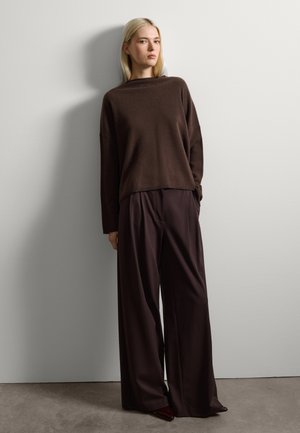 Pull en tricot marron à coupe loose et manches longues, associé à un pantalon large taille haute marron foncé. Lignes simples et épurées.