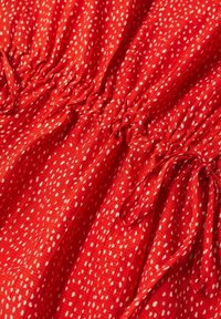 Tissu rouge avec de petites taches blanches rassemblées au centre par un élastique ou un cordon formant une texture froncée.