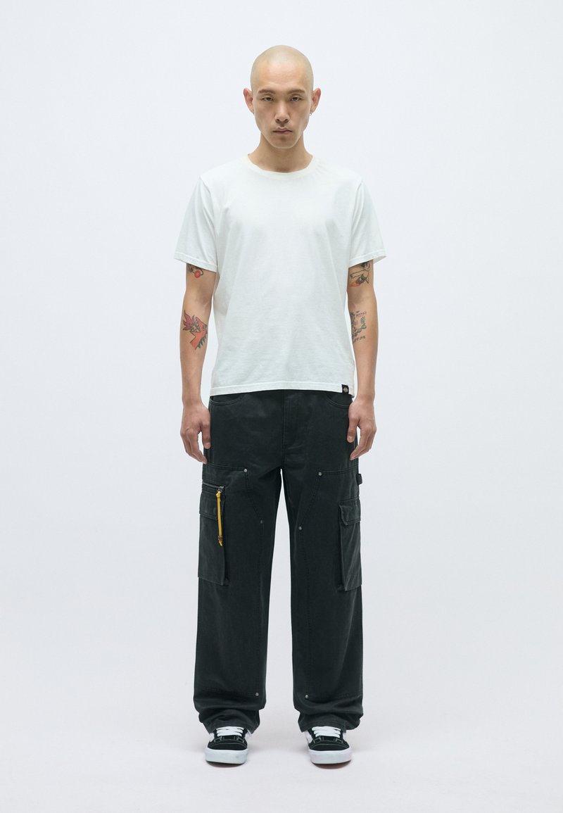 Lagani bijeli pamukasti T-shirt upareni s labavim crnim cargo hlačama koje imaju više džepova, žute detalje na zatvaraču i crne tenisice.