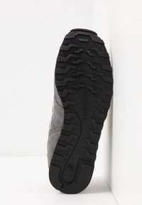 Semelle d'une chaussure New Balance grise montrant une bande de roulement en caoutchouc noir avec des motifs en zigzag et le nom de la marque embossé.