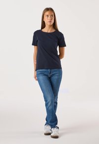 Laivastonsininen puuvillainen t-paita, jossa on lyhyet hihat, pyöreä pääntie ja rento istuvuus, yhdistetty vaaleansinisien farkkujen ja valkoisten lenkkarien kanssa.