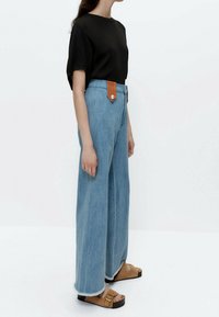 Sort ribbet kortærmet top kombineret med lyseblå, brede jeans med høj talje, som har en brun læderdetalje ved taljen, og brune sandaler.