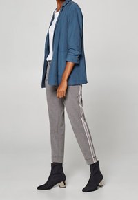 Blaues Leinenblazer, weißes T-Shirt, graue gestreifte Hose und schwarze Stiefeletten mit beige Absatz. Fokus auf klare Linien und modernen Schnitt.
