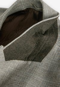 Grau karierten Mantel mit einem Wollkragen und einem glatten braunen Innenfutter, sichtbaren Nähdetails und einem strukturierten Design.