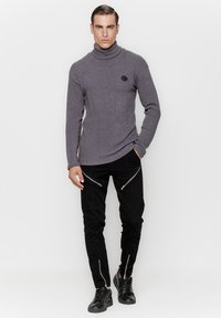 Szary sweter z golfem o żeberkowej strukturze, zestawiony z czarnymi spodniami z zamkami błyskawicznymi z przodu i przy kostkach. Czarne sneakersy dopełniają stylizację.