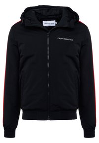 Svart huvad jacka med röda sidostripes, framdragkedja, elastiska muddar och midjeband. Har en logotyp på bröstet och är gjord av mjukt tyg.