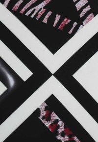 Geometrisch gemusteter Stoff mit schwarzen und weißen Segmenten, die mit roten und weißen Akzenten durchzogen sind, bestehend aus verschiedenen linearen Designs.