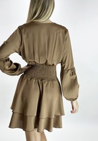 Braunes Satinkleid mit gepufften langen Ärmeln, einem gerafften Taillenbereich und mehrlagigem Rock. Glatte Textur mit fließender Silhouette.