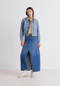 Jeansjacka med en beige sherpa-krage, tillsammans med en lång jeanskjol med en framfålla. Modellen bär mintgröna sneakers.