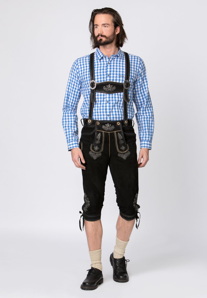Black suede lederhosen with silver embroidery, paired with a blue checkered shirt. Features shoulder straps and knee-length design. Black shoes and light socks.