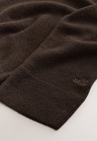 Ruskea neulottu kangas, jossa on pehmeä pinta ja pieni ommeltu logo kulmassa. Taiteltu, sileäpintainen, ilman kuvioita.