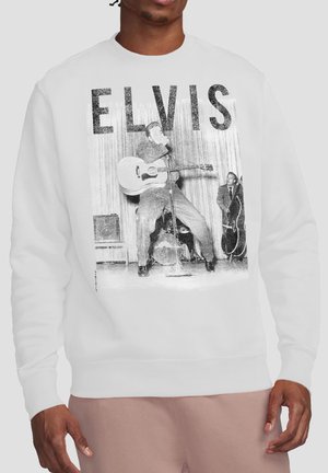 Mann trägt weißen Pullover mit schwarz-weißem Foto des Gitarristen Elvis, der mit der Band auf der Bühne auftritt, und großem "ELVIS"-Text darüber.