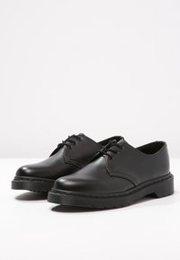 Scarpe stringate in pelle nera con finitura liscia, punta rotonda e suola in gomma testurizzata. Presentano dettagli di cucitura discreti sui lati.