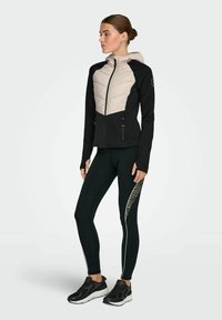 Črna in bež jakna z zadrgo spredaj, kapuco in dvema stranskima žepoma. Črne legice z leopardjim tiskom in belo stransko črto.