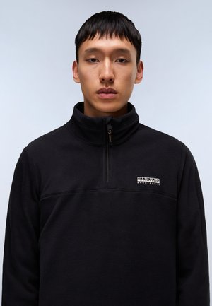 Svart fleece-pullover med høy krage, halv-glidelås design og brystlogo i hvitt. Myk tekstur og figurnær silhuett.