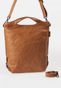 Bruine leren tote bag met een gladde textuur, unieke uitsnede handvat en verstelbare schouderriem. Zijhardware accenten voegen detail toe.