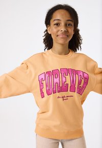 Sudadera de melocotón con cuello redondo y corte holgado, que presenta un gran texto en rosa "FOREVER" y acentos bordados. Tela suave y casual.