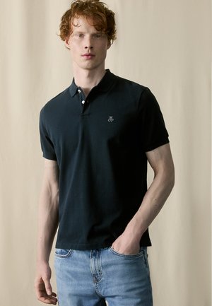 Dark navy polo shirt with a collar, short sleeves, and a small embroidered logo on the chest, paired with light blue jeans.