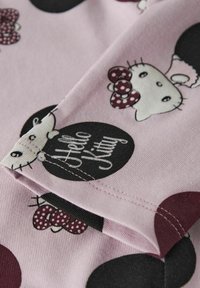 Różowa tkanina z powtarzającym się wzorem Hello Kitty, z kokardkami w groszki, czarnymi kółkami i tekstem. Miękka faktura i widoczne detale szwów.