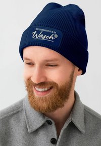 Navy knitted beanie with a ribbed texture and a contrasting patch featuring white text and a floral design.