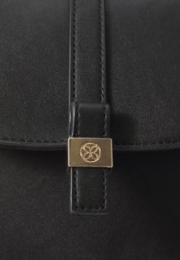 Svart läderväska med en slät yta, med en guldtonad hårdvaruknäpp och dekorativt emblemet på stängningsremmen.
