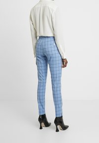 Light blue checkered trousers with a tailored fit, complemented by black patent high heels and a white long-sleeve blouse.