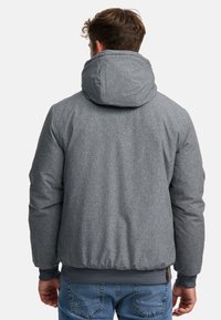 Gray quilted jacket with a hood, featuring a textured fabric, ribbed cuffs, and hem. Visible stitching and minimal branding details.