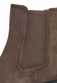 Bottine en daim brun avec un panneau latéral élastique texturé, des détails cousus et un bout arrondi. Fini lisse avec des accents minimalistes.
