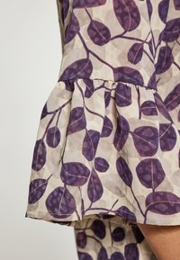 Tessuto con stampa di foglie viola e orlo svasato. La texture è leggera e leggermente trasparente, con uno sfondo crema e delicate fantasie.