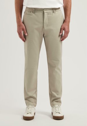 Beige katoenen broek met een rechte snit, voorzien van zijzakken, een haak-en-oogsluiting, en gedragen met witte sneakers.