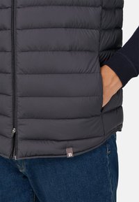 Gilet in stile bomber grigio con design trapuntato, dotato di chiusura con zip e tasche laterali. Include un'etichetta in tessuto con il logo "B" sull'orlo.