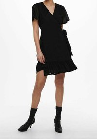 Vestito nero avvolgente con maniche a sbuffo corte, scollo a V, orlo arricciato e cintura regolabile in vita, abbinato a stivali neri alla caviglia.