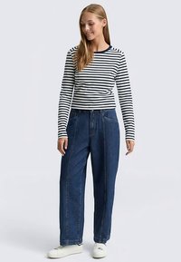 Pasiasta bluzka z długim rękawem i okrągłym dekoltem, zestawiona z luźnymi niebieskimi dżinsami i białymi trampkami. Gładka bawełniana tkanina, luźny krój.