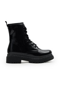 Botín de combate negro brillante con cordones, suela gruesa tipo lug, altura hasta el tobillo y un tirador en la parte trasera.