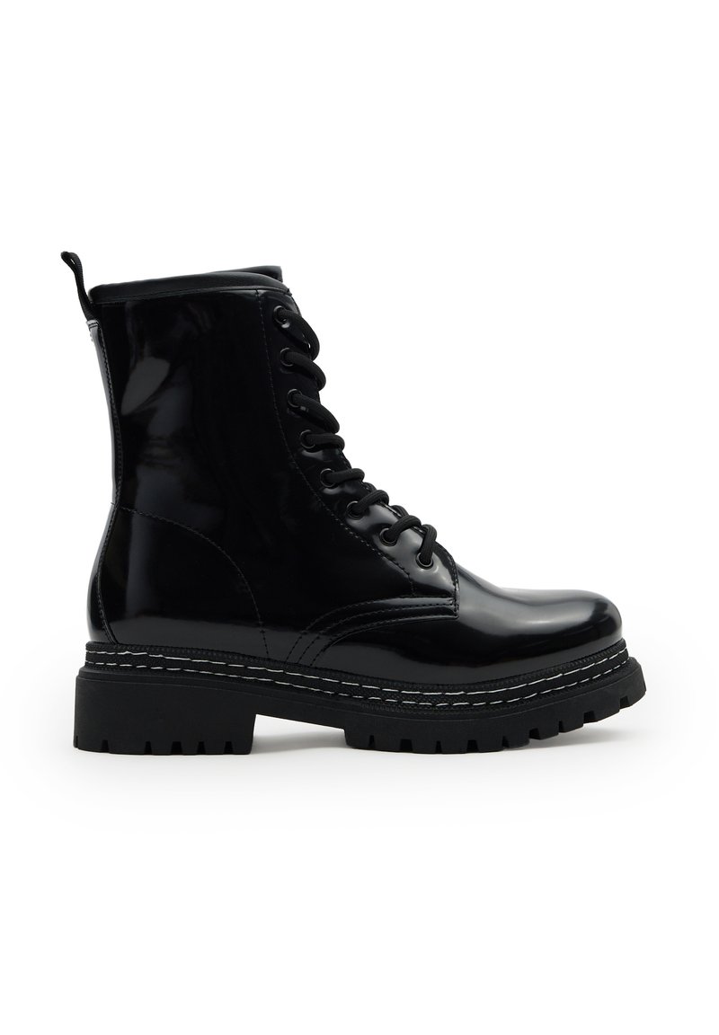 Botín de combate negro brillante con cordones, suela gruesa tipo lug, altura hasta el tobillo y un tirador en la parte trasera.