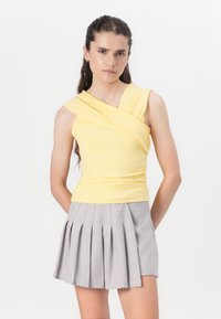Un haut jaune ajusté avec un design sur une épaule et une texture froncée, associé à une jupe plissée grise clair. Un style simple et contemporain.