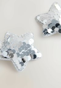 Silberne, sternförmige Verzierungen aus Pailletten, die eine glänzende Textur mit metallischem Glanz und einen genähten Rand aufweisen.