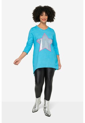 Tunique turquoise avec une grande étoile en sequins argentés et un contour rose, associée à des leggings noirs et des bottines argentées brillantes.