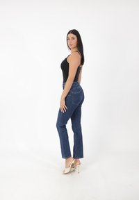 Jean skinny bleu avec poches avant et arrière, associé à un débardeur noir ajusté et des sandales à talons hauts de couleur claire.