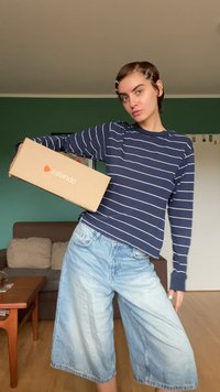 Langärmliges, gestreiftes Hemd in Marineblau, kombiniert mit hellblauen weit geschnittenen Jeansshorts. Das Model hält eine braune Zalando-Box. Schlichtes Design und lässiger Stil.