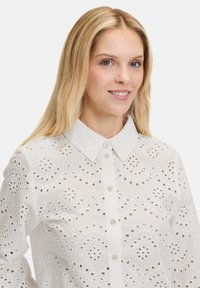 Weiße Bluse aus Broderie anglaise mit durchgehender Knopfleiste, Kragen und komplizierten kreisförmigen Mustern überall.