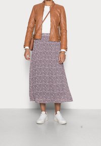 Bruine leren jas, witte top, bloemenrok tot op de knie in paarse tinten, en witte sneakers. Eenvoudig ontwerp met een casual uitstraling.