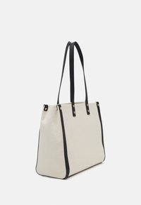 Beige canvas tote bag med svarta läderdetaljer, strukturerad design och två långa handtag. Guldiga detaljer på sidorna.