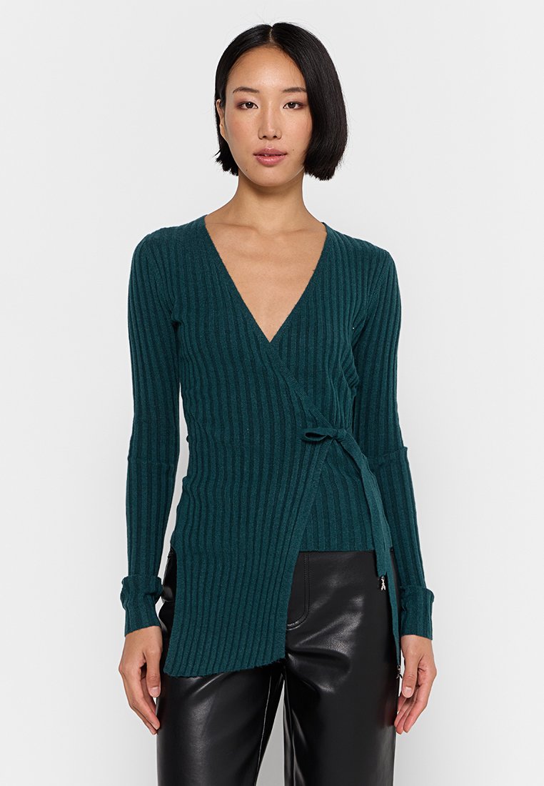 Maglioncino avvolgente color teal a coste con maniche lunghe e dettaglio annodato sul davanti, caratterizzato da un profondo scollo a V e una silhouette aderente. Tessuto morbido.