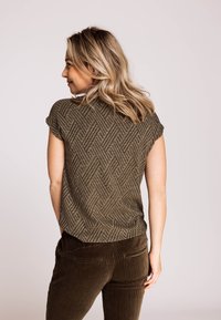 Braunes kurzärmeliges Oberteil mit gemustertem Fischgrät-Design, rundem Ausschnitt und lockerem Schnitt, kombiniert mit dunkler Cordhose.