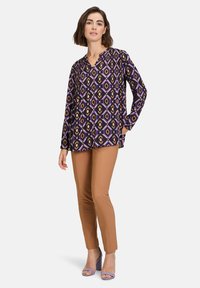 Long-sleeve top with a purple, diamond-patterned design. Paired with fitted caramel pants and purple block-heeled sandals.