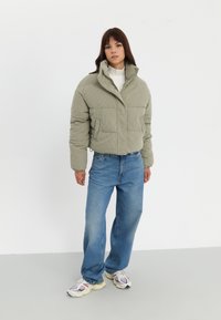 Kaki kordpuffjacka med hög krage, tryckknappar, två framfickor, i kombination med ljusblå vida jeans och chunky sneakers.