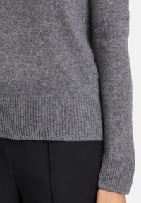 Szary sweter dzianinowy z ściągaczem na dolnym brzegu i mankietach, o miękkiej fakturze i luźnym kroju. Widoczne detale przeszycia na dole.